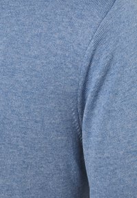 Sweter dziany w jasnoniebieskim kolorze, charakteryzujący się miękką fakturą i gładkim wykończeniem. Szwy na ramieniu dodają subtelnej elegancji.