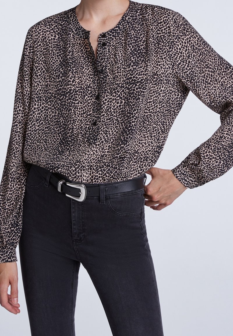 Leopardenmuster-Bluse aus leichtem Material, mit Knopfausschnitt und langen Ärmeln, kombiniert mit schwarzen Jeans und einem schwarzen Gürtel.