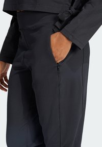 Zwarte sportbroek gemaakt van rekbare stof, met een ritszak, gestikte naden en een nauwsluitende pasvorm rond de taille en benen.