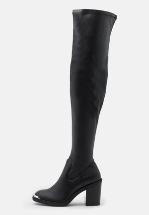 Bottes noires au-dessus du genou en cuir lisse, présentant un bout rond, un talon épais et un accent métallique sur le bout de la chaussure.