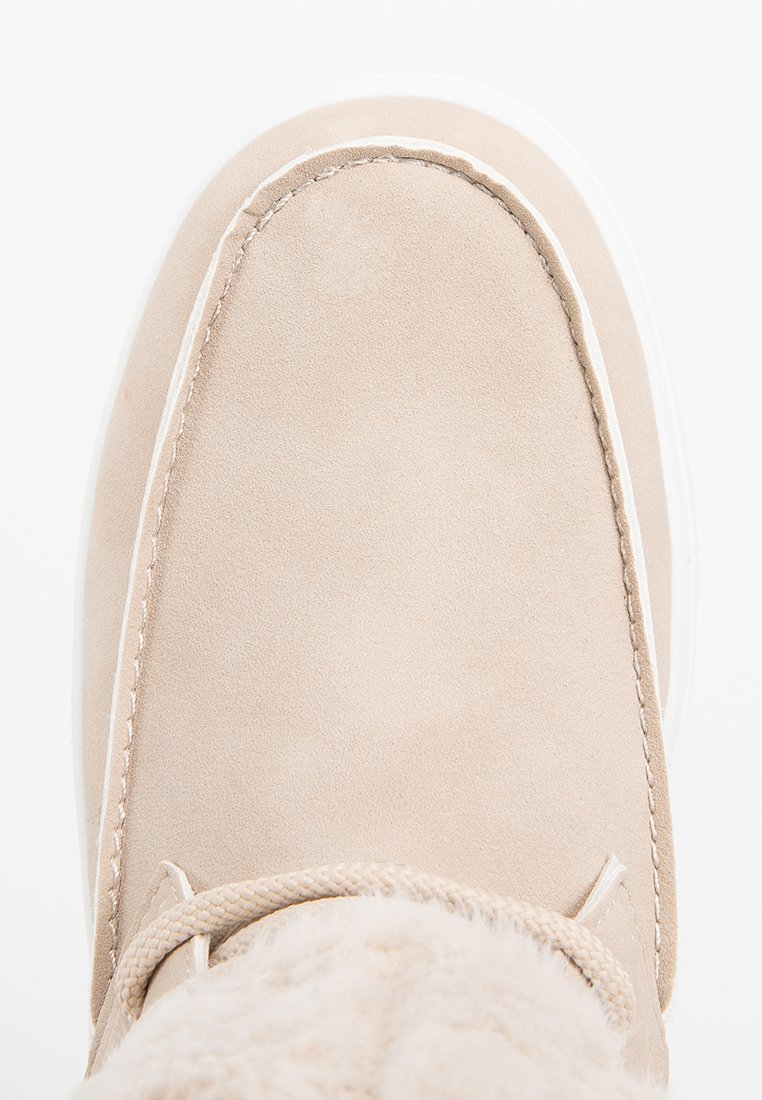 Bottines en suede beige avec un bout rond, une semelle blanche et une doublure en fourrure. Coutures détaillées le long du bord et laçage à l'avant.