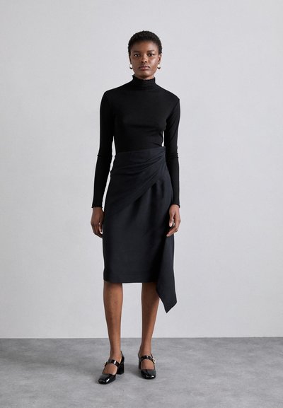 Top a collo alto nero abbinato a una gonna avvolgente a vita alta. La gonna presenta un orlo asimmetrico e un tessuto liscio. Completato con scarpe in vernice.