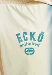 Svetlá tkanina s prechodom do teal farby, obsahujúca text "ECKŌ unlimited" a obrys nosorožca. Hladký povrch.