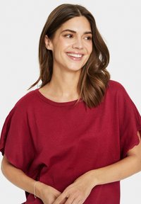 Haut court rouge à manches courtes avec une coupe ample et un tricot texturé. Encolures lisses et manches légèrement drapées créent une silhouette décontractée.