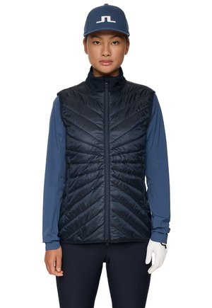 Marineblauer Steppweste mit hohem Kragen, diagonalem Chevron-Muster, Reißverschluss und einem blauen Langarmhemd darunter.