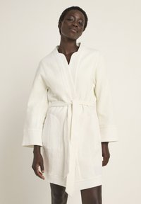 White textured robe with a deep V-neck, long sleeves, and a tie waist. Features two front pockets and a slightly loose fit.