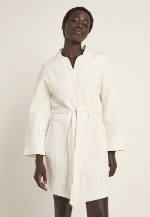 White textured robe with a deep V-neck, long sleeves, and a tie waist. Features two front pockets and a slightly loose fit.
