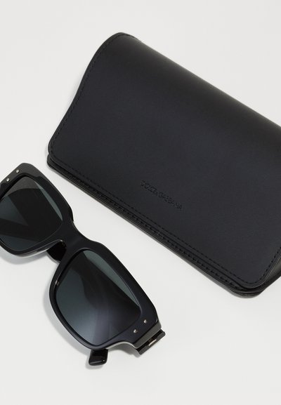 Black rectangular sunglasses with dark lenses, resting next to a black leather case embossed with "Dolce & Gabbana." Smooth texture, minimal design.