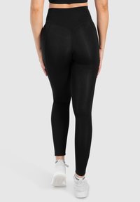 Leggings noirs taille haute en matériau extensible, avec une texture lisse, une coupe ajustée et des détails de couture subtils.