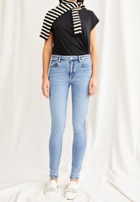 Úzké džíny z světle modrého denimu, s pasem ve střední výšce a přiléhavým střihem. Kombinované s černou košilí a černo-bílým pruhovaným svetrem.