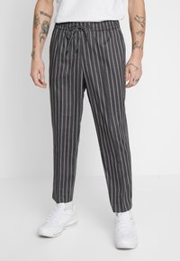 Harmaat raidalliset housut, joissa on joustava vyötärö ja nauhakuja, sekä kapeneva lahkeiden muotoilu. Yhdistetty valkoisiin urheilukenkiin.