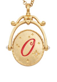 Necklace u zlatnom tonu s okruglim privjeskom na kojem se nalazi uzdignuto crveno slovo "O", ukrašen malim biserima i ugraviranim zvjezdicama.
