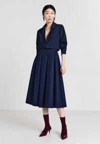 Blusa blu navy con bottoni e maniche lunghe abbinata a una gonna midi plissettata a vita alta, completata da scarpe con tacco borgogna e calze.