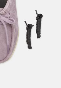 Zapato de ante morado claro con superficie texturizada y suela beige de contraste, acompañado de dos cordones negros enrollados.