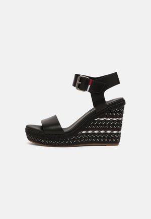 Sort kileformet sandal med ankelrem, sølvspænde og mønstret platformsål med hvide og sorte vævede detaljer.