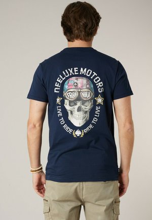 Man draagt een donkerblauw T-shirt met een schedel die een versierde helm en een bril draagt, met de tekst "Free Soul," en de teksten "Deeluxe Motors" en "Live to Ride."