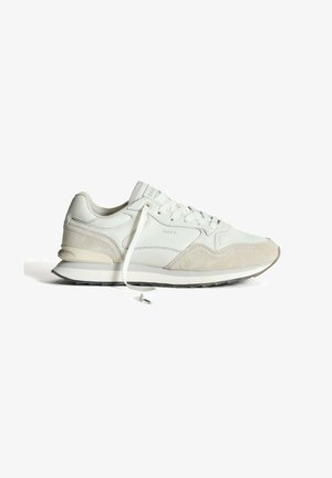 Zapatilla blanca que combina materiales de cuero y ante, con puntera redondeada, sistema de cierre de cordones y una suela en capas con una suela exterior negra contrastante.