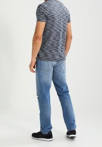 Šedé tričko s krátkým rukávem a texturovaným vzorem, kombinované se světlomodrými džínami s efektem opotřebení a černými sportovními botami.