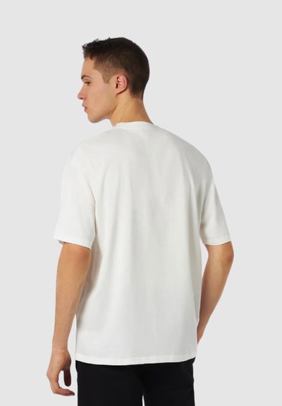 T-shirt bianco in cotone con maniche corte, vestibilità rilassata, scollo rotondo classico e texture liscia. Nessun motivo o accento visibile.