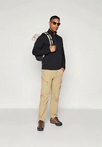 Melnas garām piedurknēm krekls, beigu krāsas bikses ar rāvējslēdzēju, brūni pārgājiena zābaki un tumši saulesbrilles. Individuāls tur mugursomu ar vieglām siksnām.