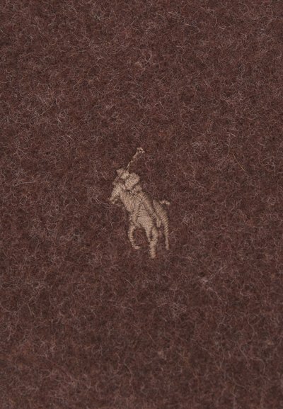 Rudas vilnos audinys turi tekstūruotą paviršių, o centre yra mažas, siuvinėtas kreminės spalvos polo žaidėjo logotipas.