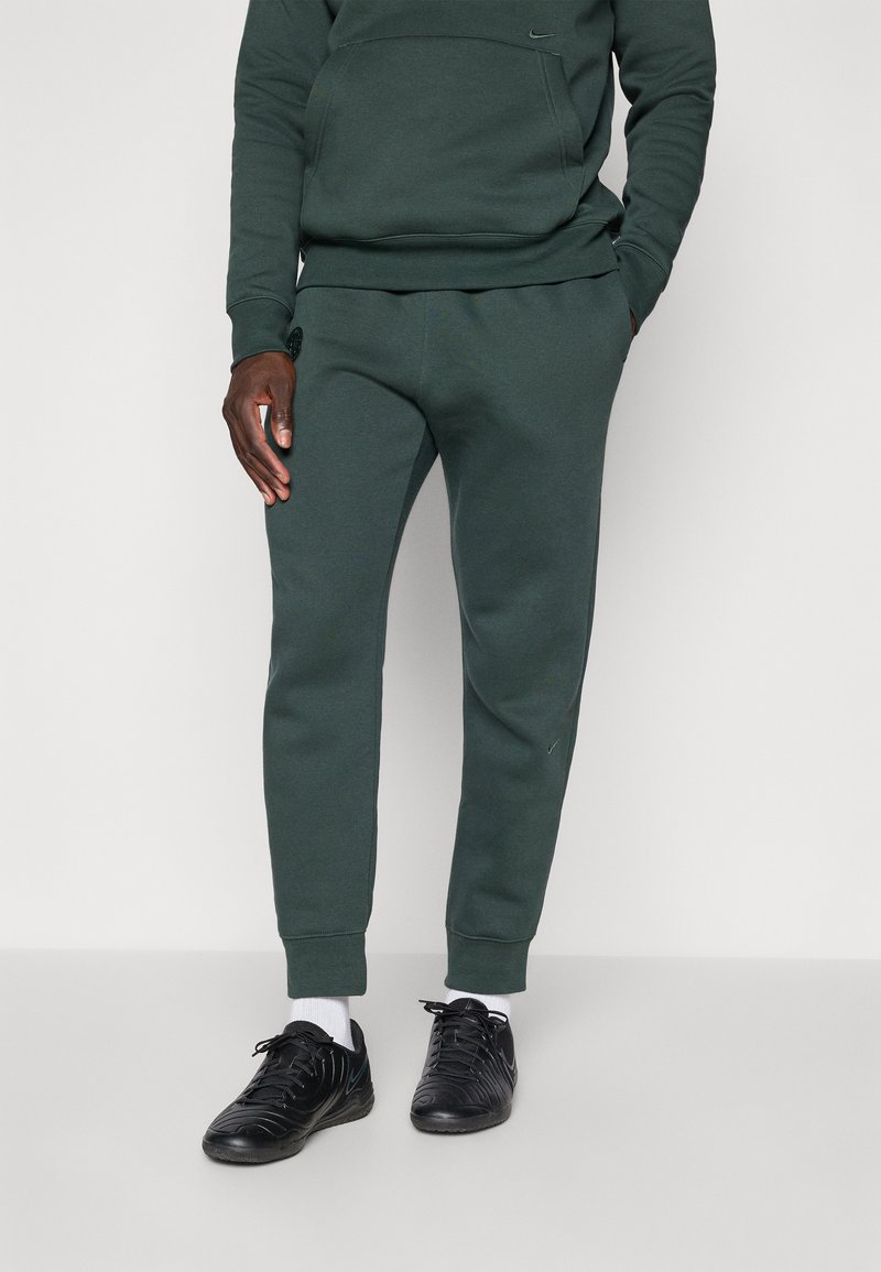 Mørkegrønne joggebukser med slim fit, laget av mykt stoff, med elastisk midje og ankelmansjetter, sammen med svarte treningssko.