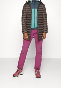 Brun vadderad jacka, teal och marinblå lager-på-lager-top, lila byxor och flerfärgade sneakers. Texturerade material och sportig, funktionell design.