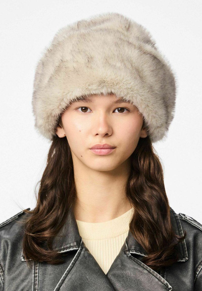 Kapa od umjetnog krzna svijetlosmeđe boje s širokim, zaobljenim obodom. Mekana tekstura s suptilnim sjajem i debelim, luksuznim izgledom.