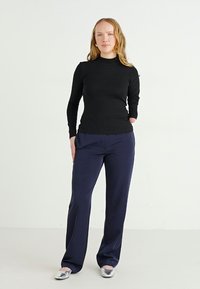 Black long-sleeve top paired with navy wide-leg trousers and shiny silver flats, set against a white background. Neat, form-fitting design.