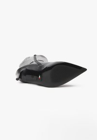 Bottine en cuir noire à bout pointu avec fermeture éclair latérale, texture visible de la semelle, et petit talon, photographiée depuis l'avant en bas.