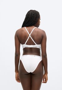 Biely bavlnený set s braletkou a tangami, s prekríženými ramienkami na chrbte a elastickými pásmi s logom. Hladká textúra, minimalistický dizajn, základný štýl spodnej bielizne.