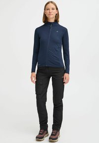 Navy long-sleeve zip-up jacket with a textured pattern, paired with black cargo pants featuring pockets and brown hiking boots.