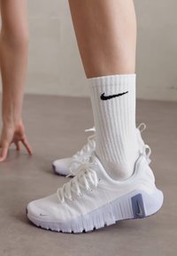 Valged Nike tossud tekstureeritud disainiga ja lilla aktsentidega, koos ribakujuliste valgete sokkidega, millel on must logo.