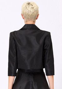 Veste noire cropped en satin. Présente un col classique et des manches trois quart, avec une texture lisse et des détails de couture à l'arrière.
