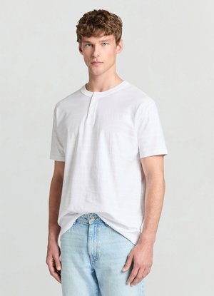 Weißes Henley-Hemd mit kurzen Ärmeln, strukturiertem Streifenmuster, dreiknöpfiger Knopfleiste und lockerem Schnitt, kombiniert mit hellblauen Jeans.