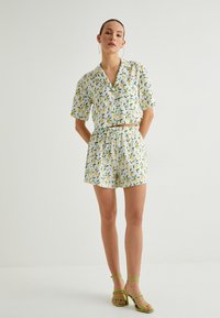 Ensemble de chemise courte à manches courtes et de shorts avec motif de feuilles et de citrons, fond blanc, taille élastique, associé à des sandales vertes à lanières.