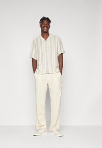Korte mouwen, gestreept shirt in beige en lichtblauw; crèmekleurige cargobroek met zijzakken; grijze sneakers met witte strepen.