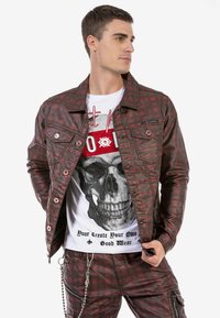 Braune karierte Jacke mit silbernen Beschlägen, Fronttaschen, kombiniert mit einem weißen T-Shirt, das ein schwarzes Schädelmotiv und schwarzen Text trägt.