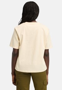 Béžové bavlněné tričko s volným střihem, krátkými rukávy a jednoduchým kulatým výstřihem, zobrazené ze zadní strany s minimálním detailem.