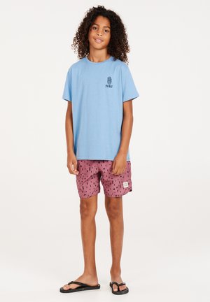 Lichtblauwe katoenen T-shirt met een bedrukt logo, gecombineerd met roze zwembroek met een zwart abstract patroon. Zwarte flip-flops.