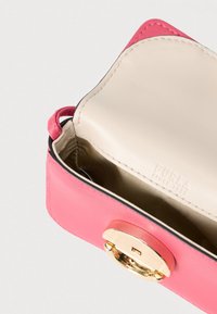 Rózsaszín bőr kézitáska arany színű, kör alakú kapoccsal, bézs belső béléssel és a márka dombornyomott logójával, amely belül látható. Simább felület.