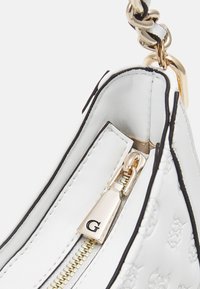 Vit läderhandväska med svarta detaljer, utrustad med dragkedja och guldkedja som handtag. Den strukturerade ytan visar ett subtilt mönster.