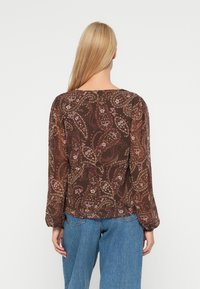 Rjava bluzica s dolgimi rokavi, okrašena z vzorcem paisley v roza in smetani barvi. Hrbtna stran ima ravno izrez in nabrane manšete.