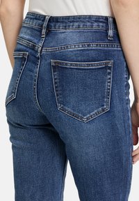 Blauwe denim jeans met een medium taille, vijf-pocket ontwerp en contrasterende stiksels. De stof heeft een gestructureerde afwerking met lichte vervaging.