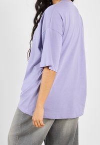 Camiseta de manga corta de gran tamaño en algodón de lavanda clara con un corte relajado y cuello redondo, combinada con pantalones gris holgados.