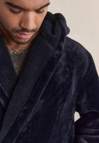 Navy blue fleece robe with a soft texture, featuring a hood and shawl collar. Close-up of the material's plush surface and stitching details.