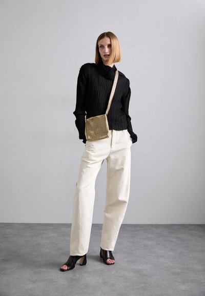 Chemise noire à manches longues côtelées, pantalon large crème, talons ouverts noirs et sac bandoulière métallique doré. Textures lisses et formes structurées.