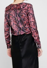 Langärmliges Hemd im rosa-schwarzen Schlangenprint-Muster, mit Rundhalsausschnitt und Knopfmanschetten, kombiniert mit einem schwarzen Satinrock.