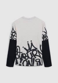 Koszula z długim rękawem w jasnym kremowym kolorze z czarnym nadrukiem w stylu graffiti na rękawach i dole, z luźnym krojem i okrągłym dekoltem.