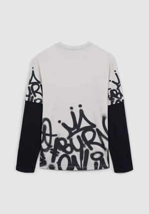 Maglietta a maniche lunghe di colore crema chiaro con stampa in stile graffiti nera sulle maniche e sul fondo, caratterizzata da un taglio casual e scollatura a girocollo.